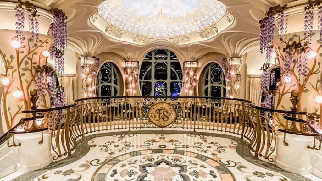 東京ディズニーシー・ファンタジースプリングスホテルの豪華なロビーエリア。吹き抜けの天井からは豪華なシャンデリアが下がり、柱には紫色の藤の花を模した装飾が施されている。2階のバルコニーの欄干にはホテルのロゴがある。