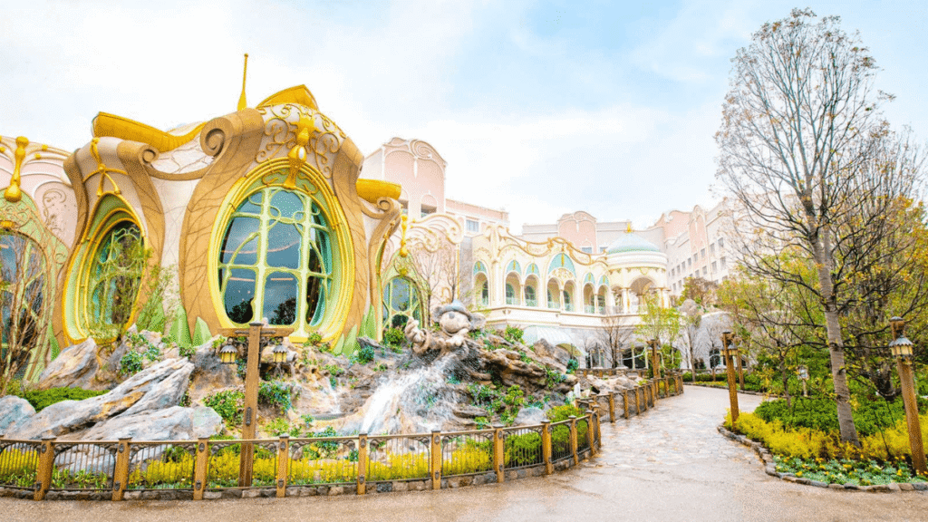 東京ディズニーシー・ファンタジースプリングスホテルの外観。パステルピンクの建物に、アールヌーボー調の植物の装飾が施された大きな窓が特徴。手前にはミッキーマウスの像と噴水がある美しい庭園が広がる。