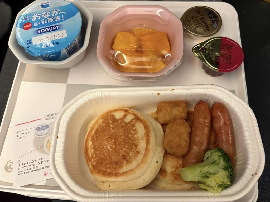 JAL機内食のリコッタパンケーキ。ポークソーセージ、ミニハッシュブラウン、ブロッコリー添えにメープルシロップとホイップバター付き