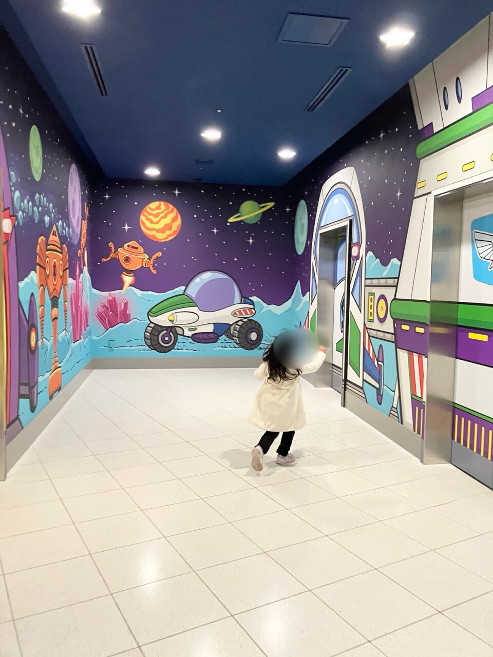 宇宙をテーマにした壁アートが描かれたトイ・ストーリーホテルのエレベーターホールと歩く子ども