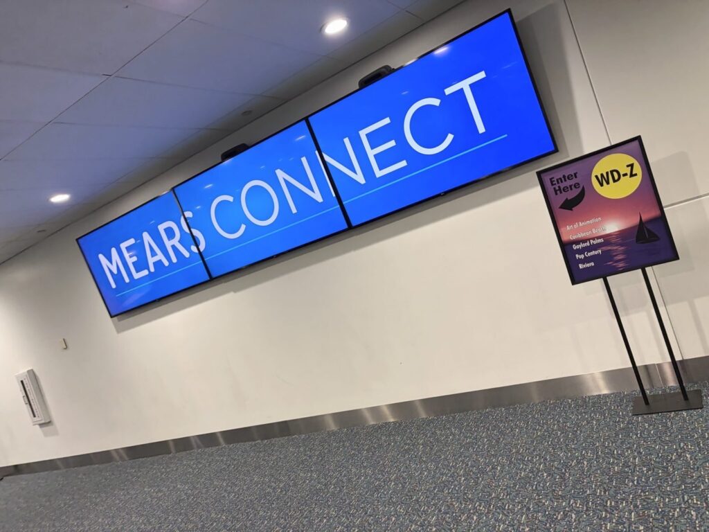 オーランド国際空港のミアーズコネクト乗り場。青い大型デジタルサイネージにMEARS CONNECTと表示され、隣の案内板には行き先ホテル一覧とEnter Hereの矢印、乗り場番号WD-Zが書かれている