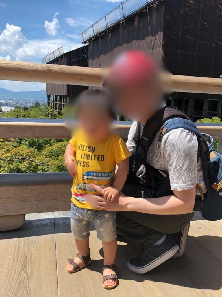 Parent and toddler on the wooden stage of Kiyomizu-dera with Kyoto city views, during the temple's famous roof renovation.
