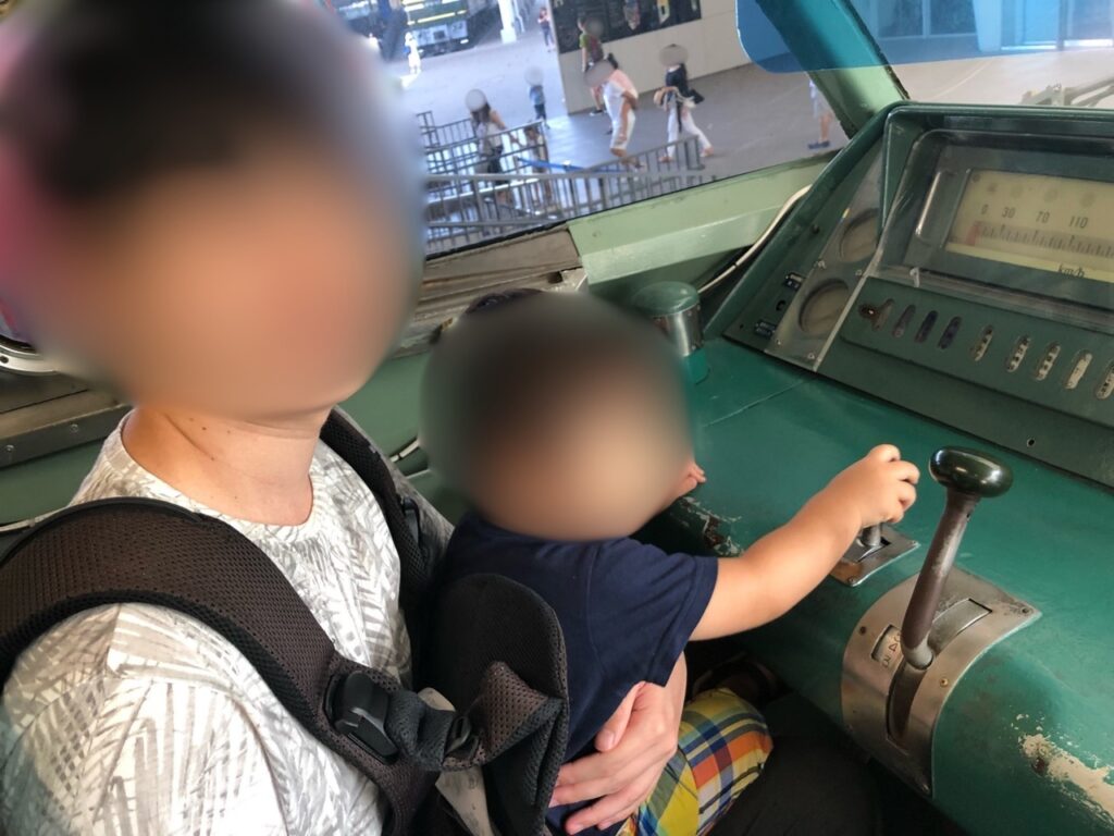A toddler sitting in the driver's cab of a real train at Kyoto Railway Museum, gripping the master controller lever.