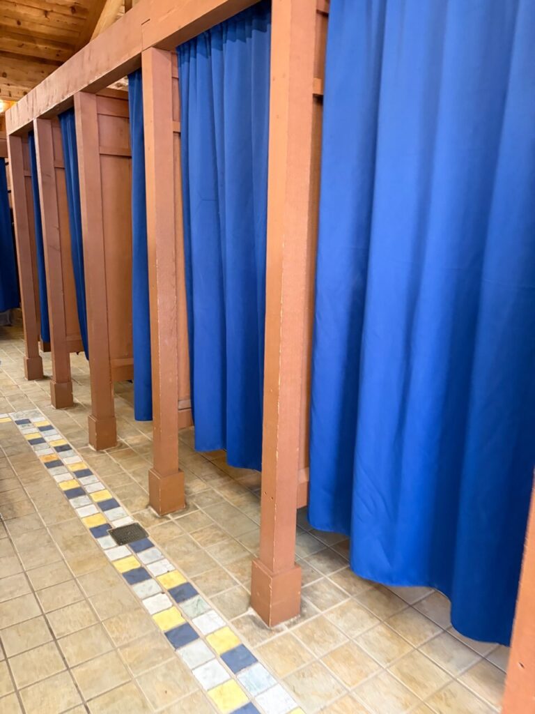 ブリザードビーチの更衣室の内部。青いカーテンで仕切られた個室がタイル床の通路沿いに並んでいる