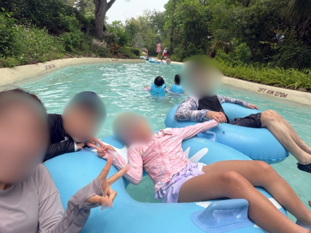ブリザードビーチの流れるプールで、青い浮き輪に乗って並んで流れる家族4人。全員が長袖ラッシュガードを着ている