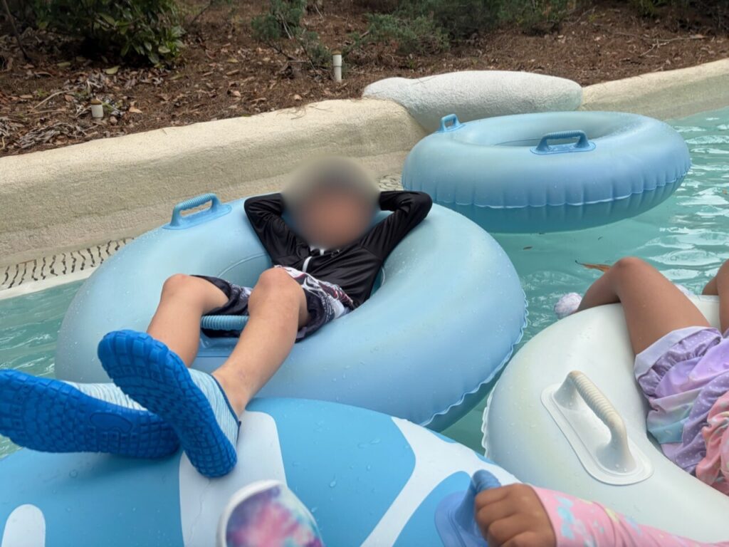 ブリザードビーチの流れるプールで、浮き輪に頭をあずけてくつろぐ子ども。足元は青いウォーターシューズ