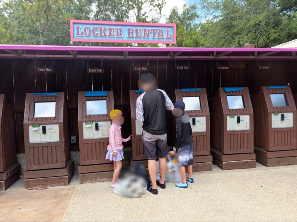 ブリザードビーチのロッカーレンタル受付。「LOCKER RENTAL」の看板の下に木製の操作機が6台並び、家族が操作している
