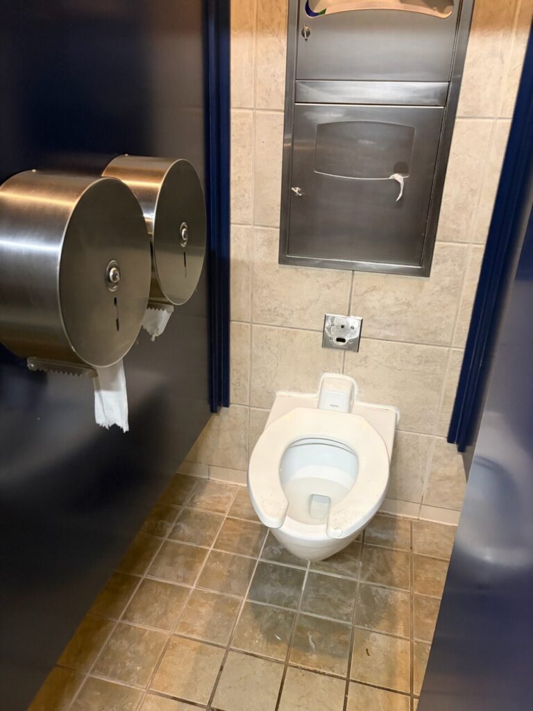 ブリザードビーチのトイレの個室。洋式便座と大きなトイレットペーパーホルダーがあり、床はプールの水で濡れている