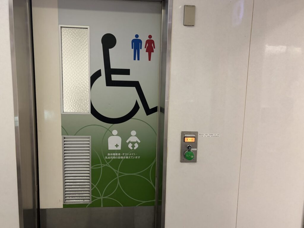 近鉄奈良駅の改札外にある多機能トイレの入口。車椅子マークとおむつ替え・オストメイトの表示がある緑色の扉