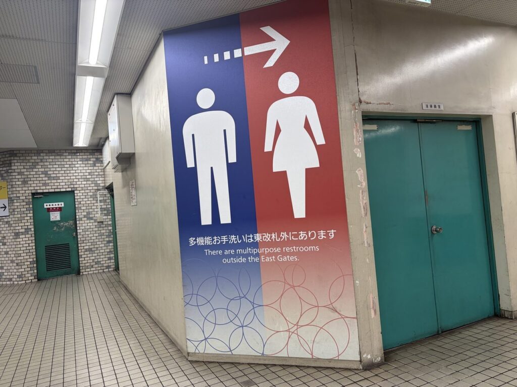 近鉄奈良駅の柱に描かれた大きな案内。男女のピクトグラムと矢印、「多機能お手洗いは東改札外にあります」の文字