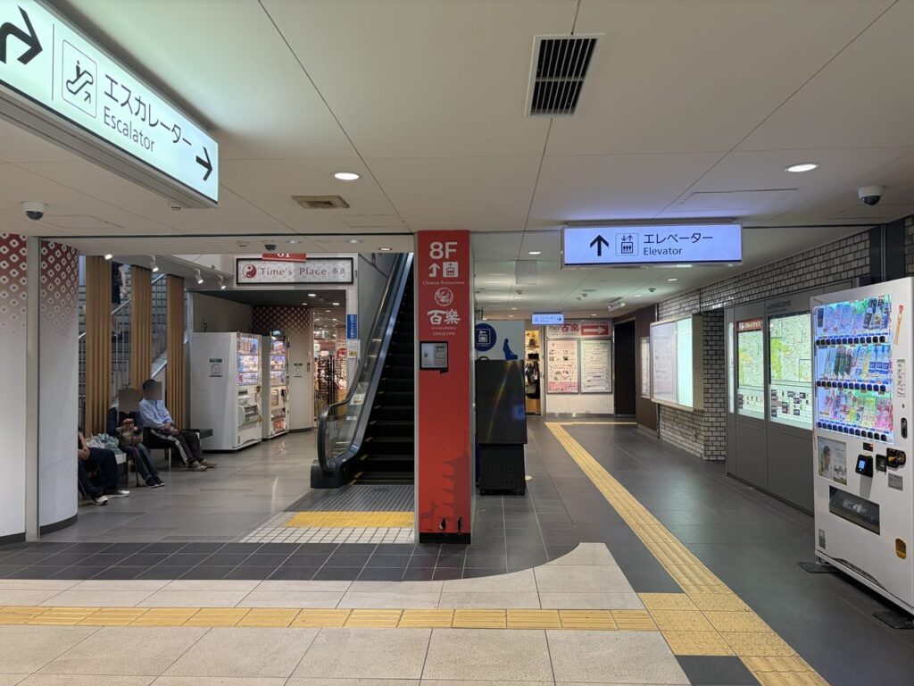 近鉄奈良駅の改札外の通路。手前にエスカレーターの案内板、奥に「エレベーター」と書かれた青い案内板が見える