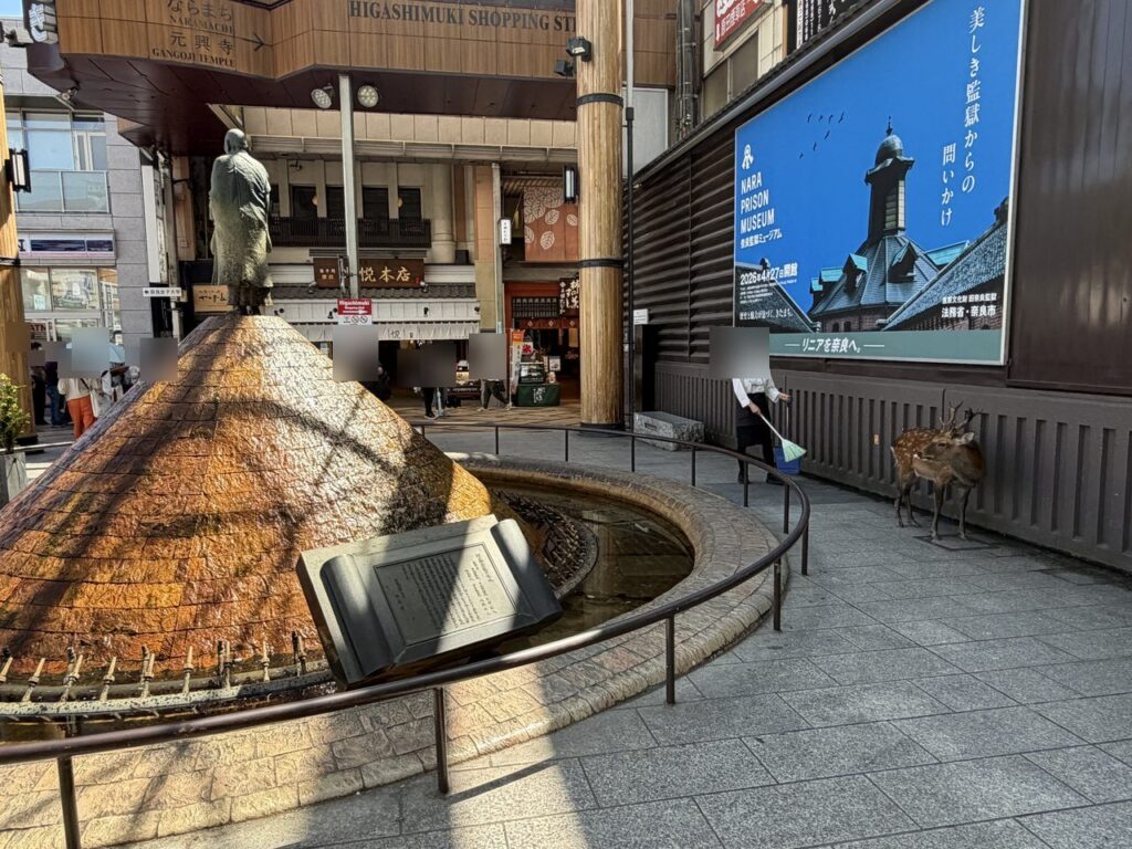 近鉄奈良駅前の噴水と、そのすぐ横の歩道に立つ1頭の鹿。奥は東向商店街の入口