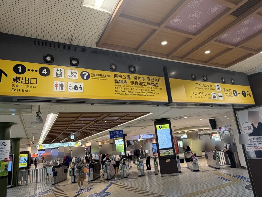 近鉄奈良駅コンコースの黄色い吊り下げ案内板。東出口1〜4、奈良公園・東大寺・春日大社・興福寺・奈良国立博物館、コインロッカー、バス・タクシー西出口5〜7が並んでいる