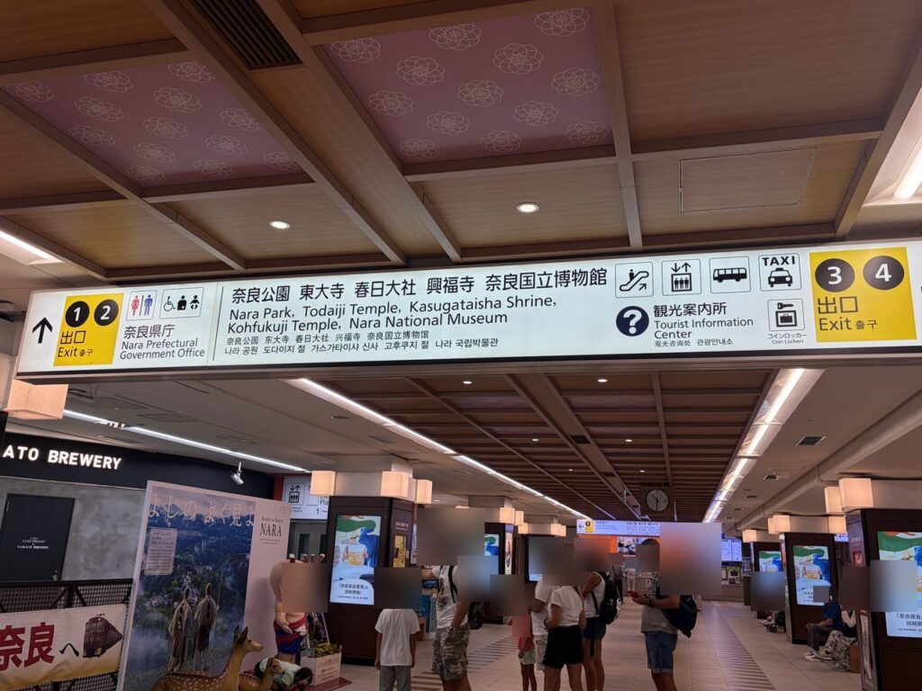 近鉄奈良駅の黄色い吊り下げ案内板。左に出口1・2(奈良県庁)、中央に奈良公園・東大寺・春日大社・興福寺・奈良国立博物館、右に出口3・4とエスカレーター・エレベーターのマーク