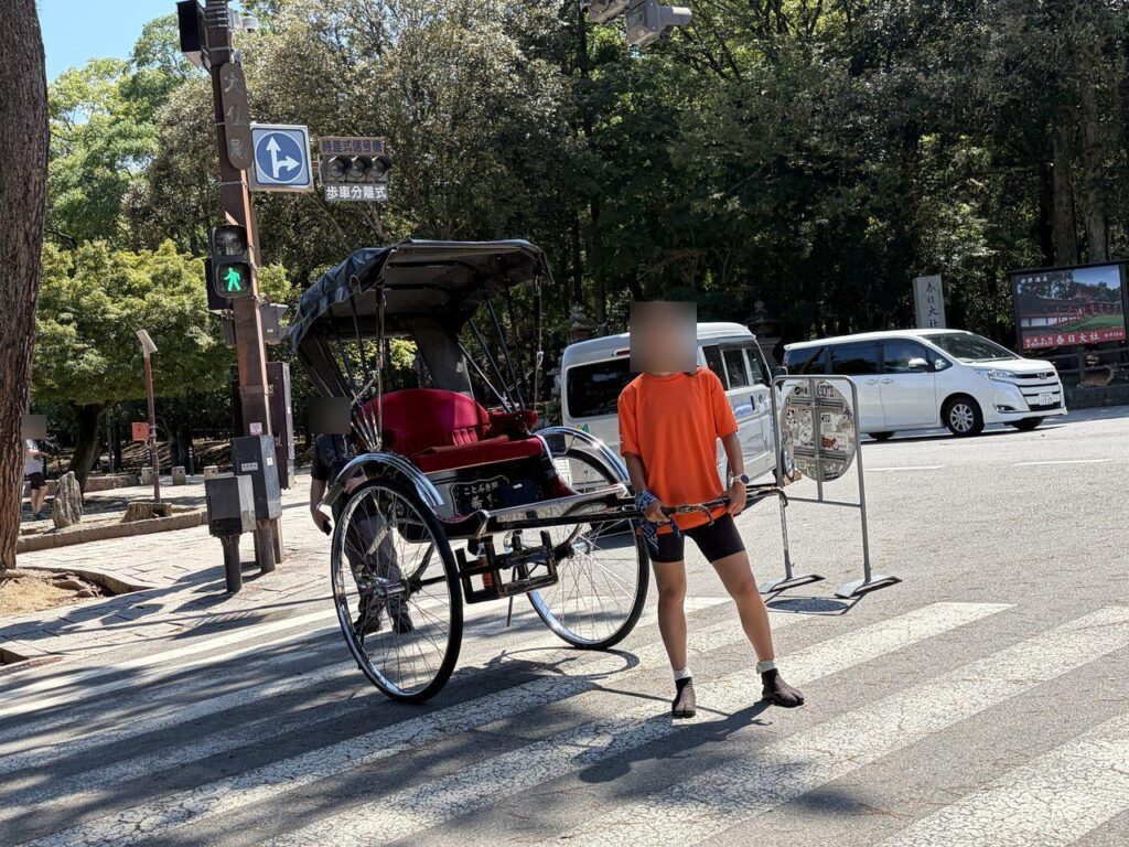 奈良公園の横断歩道を渡っていく人力車と車夫。車体に「ことぶき屋」と書かれている