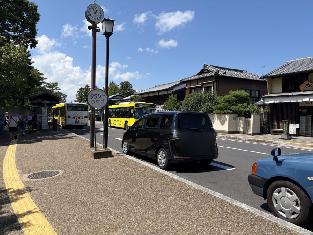 奈良公園前の道路沿いにある「タクシーのりば」の標識と、奥のバス停に停まる黄色いバス