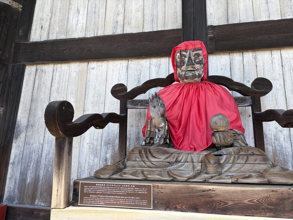 東大寺大仏殿の外に置かれたびんずる尊者の木像。赤い布をまとって椅子に座っている