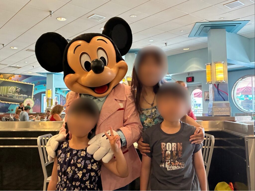 ハリウッド・アンド・バインのキャラクターダイニングで、ミッキーマウスと一緒に写真を撮る親子3人(顔はぼかし処理)。
