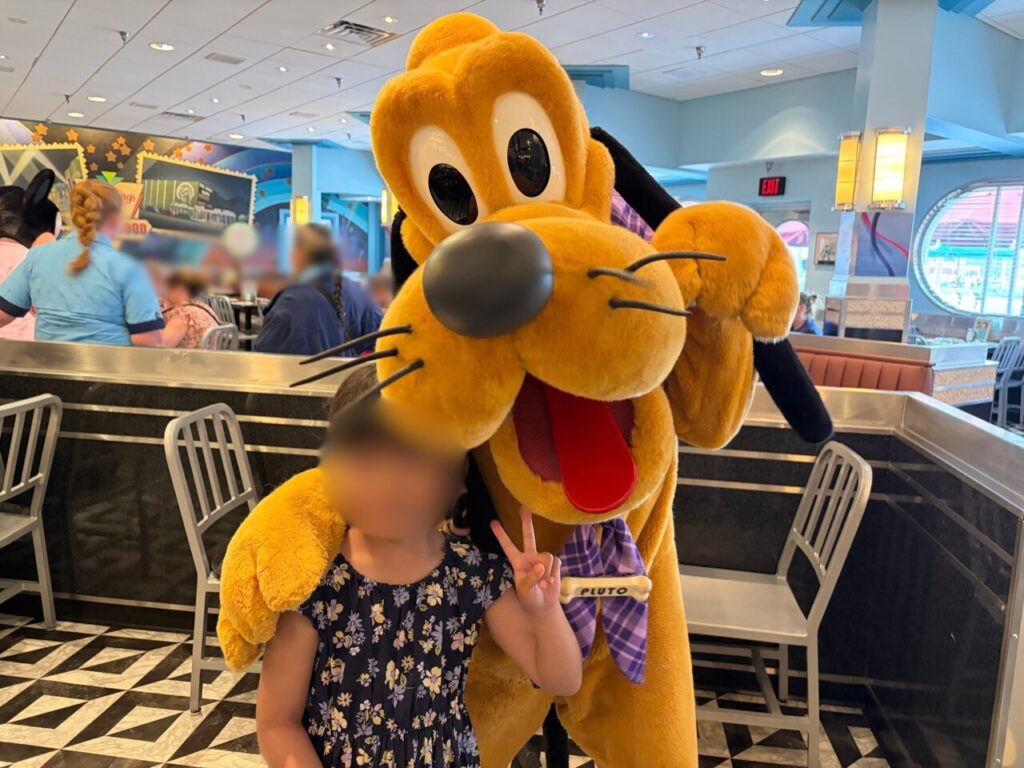 ハリウッド・アンド・バインのキャラクターダイニングで、プルートとピースサインをする子ども(顔はぼかし処理)。