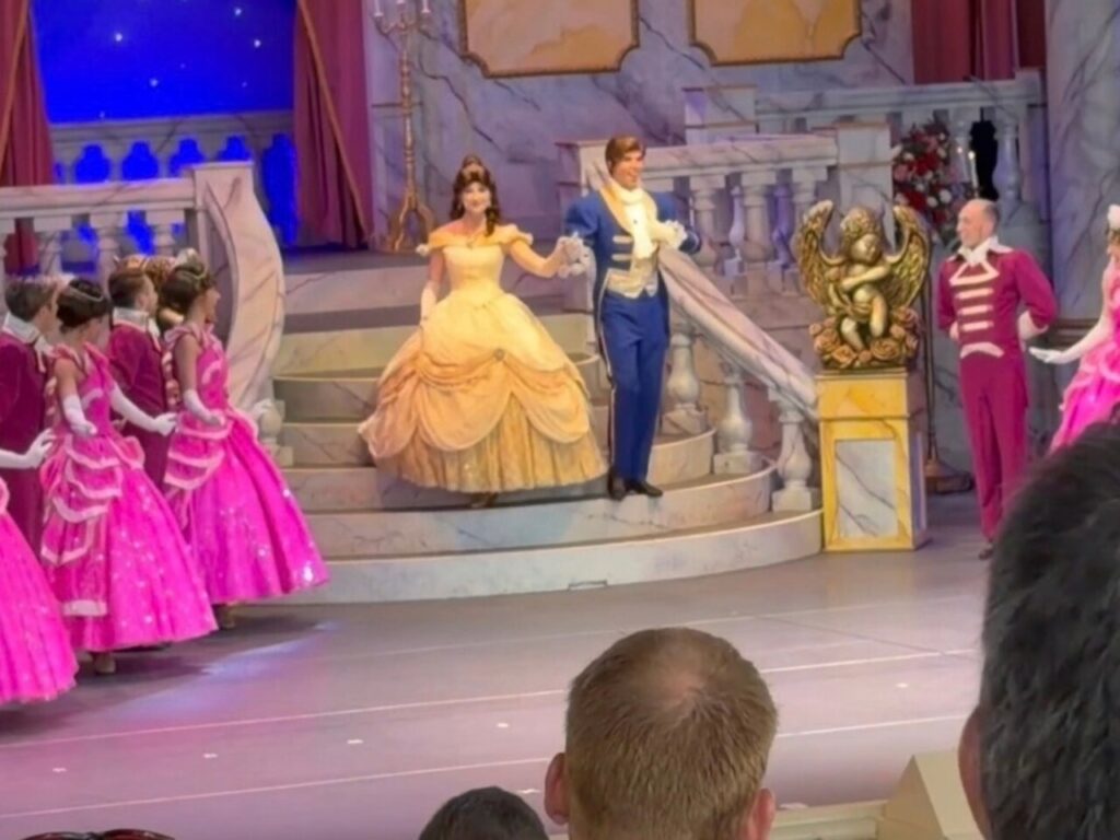 美女と野獣ライブ・オン・ステージの舞台。黄色いドレスのベルと青い衣装の王子が階段の前に立ち、ピンクのドレスのダンサーが囲んでいる。