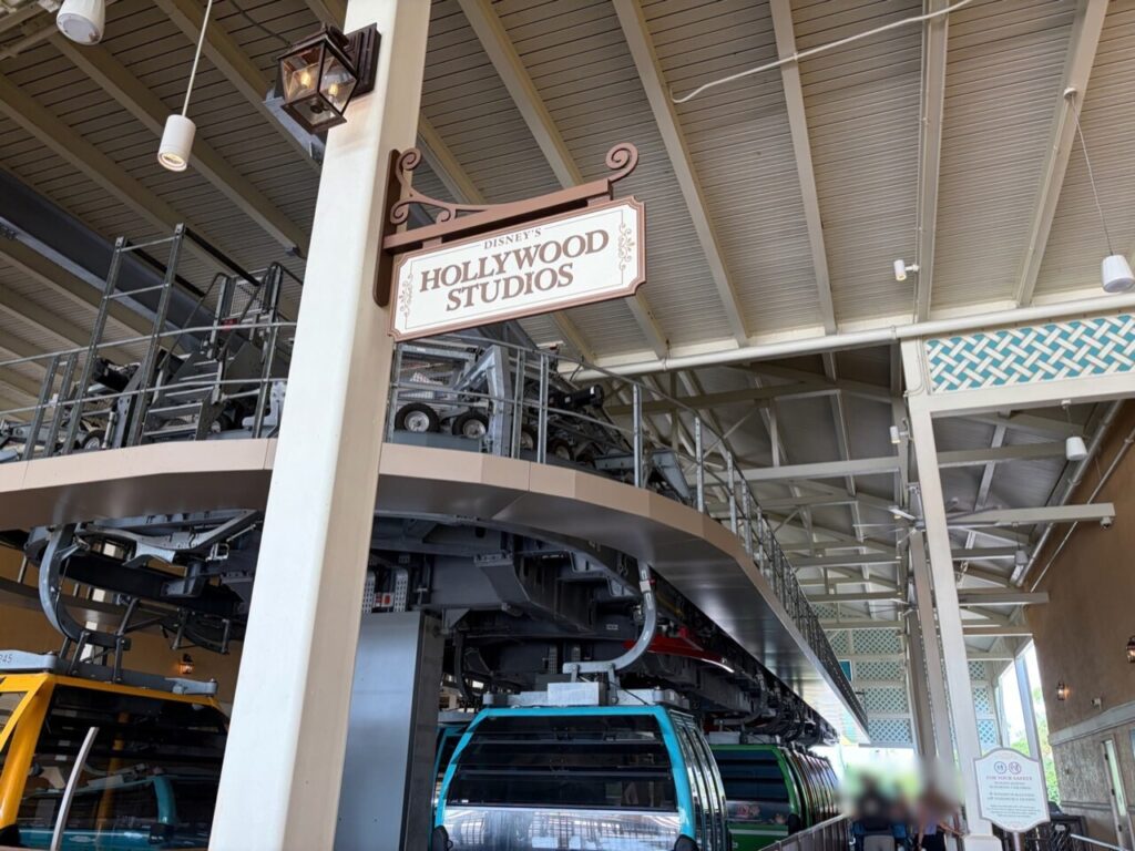 カリビアンビーチ駅のホームに掲げられた「DISNEY'S HOLLYWOOD STUDIOS」の吊り看板と、停車中の水色と緑のゴンドラ。