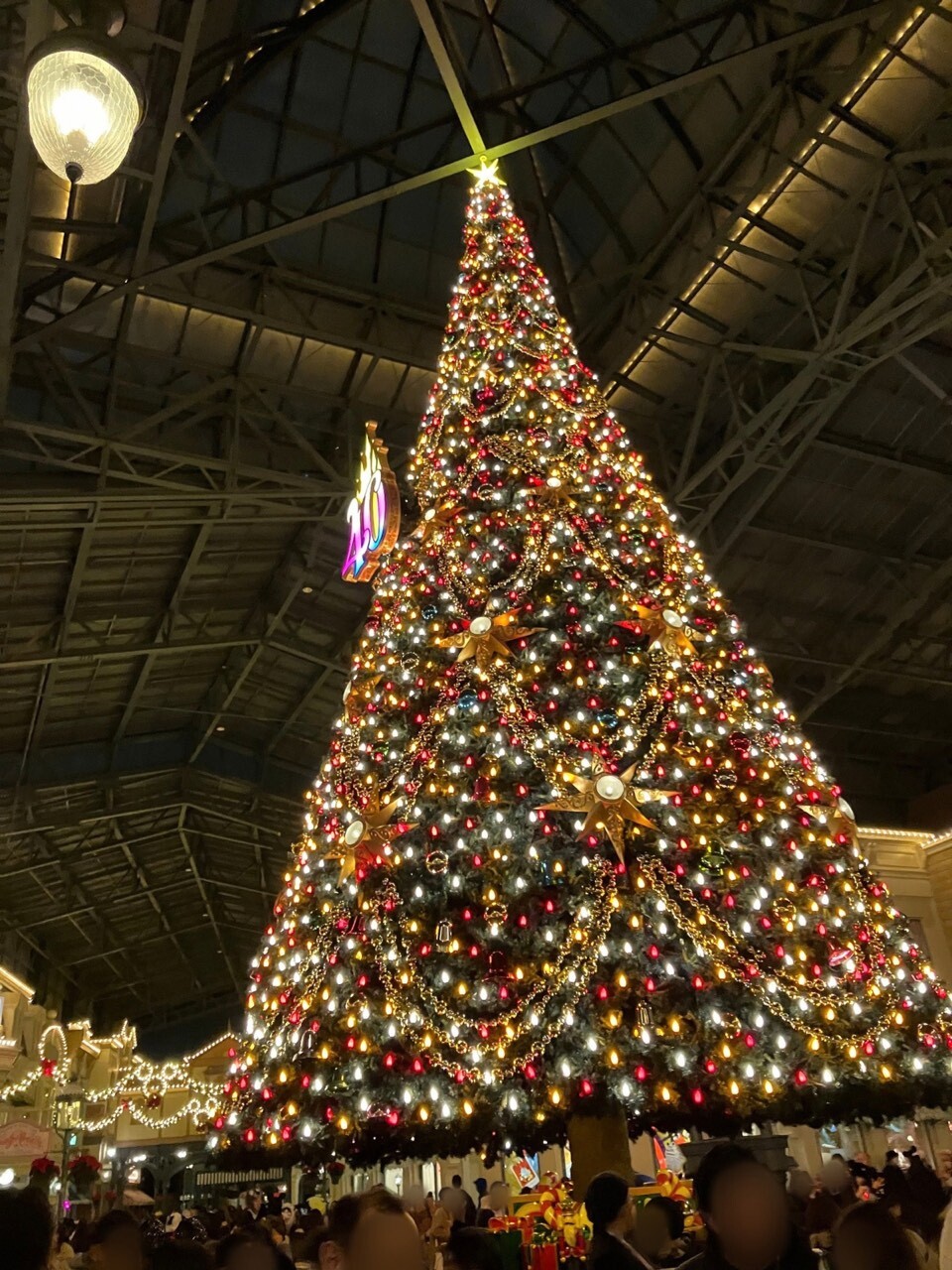 The giant Christmas tree inside World Bazaar at Tokyo Disneyland, lit up at night with red and gold ornaments